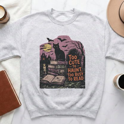 Grey sweatshirt with black cat, books, gravestone, and text "Too cute to haunt, too busy to read."