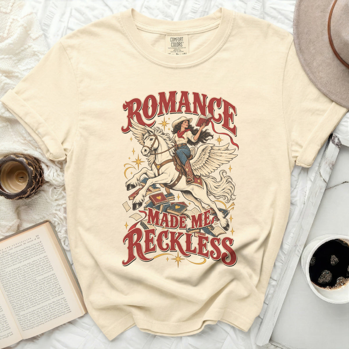 Cream t-shirt with "Romance Made Me Reckless" graphic of woman on winged horse.