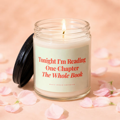 A lit glass candle with a black lid rests on a peach surface surrounded by pink flower petals.