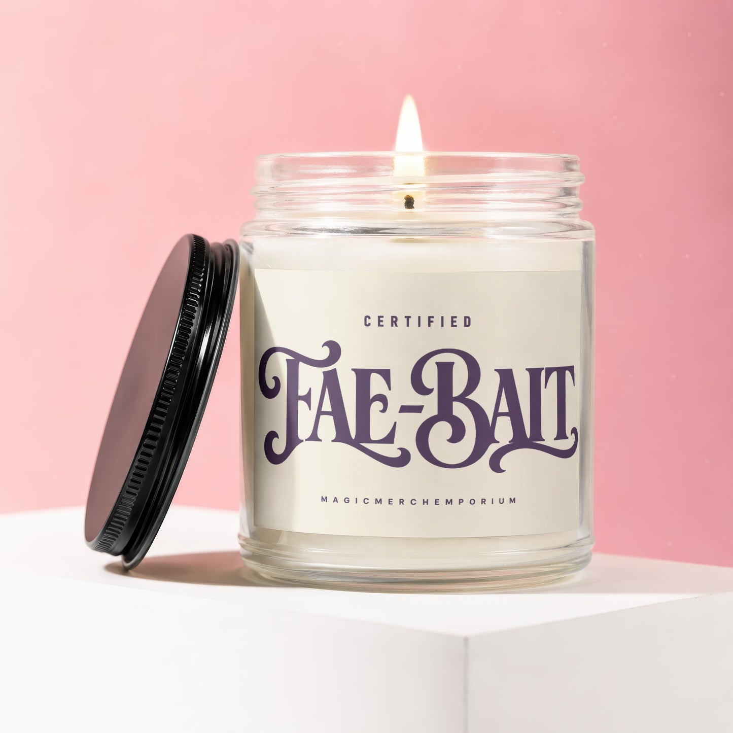 Glass jar candle labeled "Fae-Bait Certified MagicMerchemporeum" with lit wick and black lid.