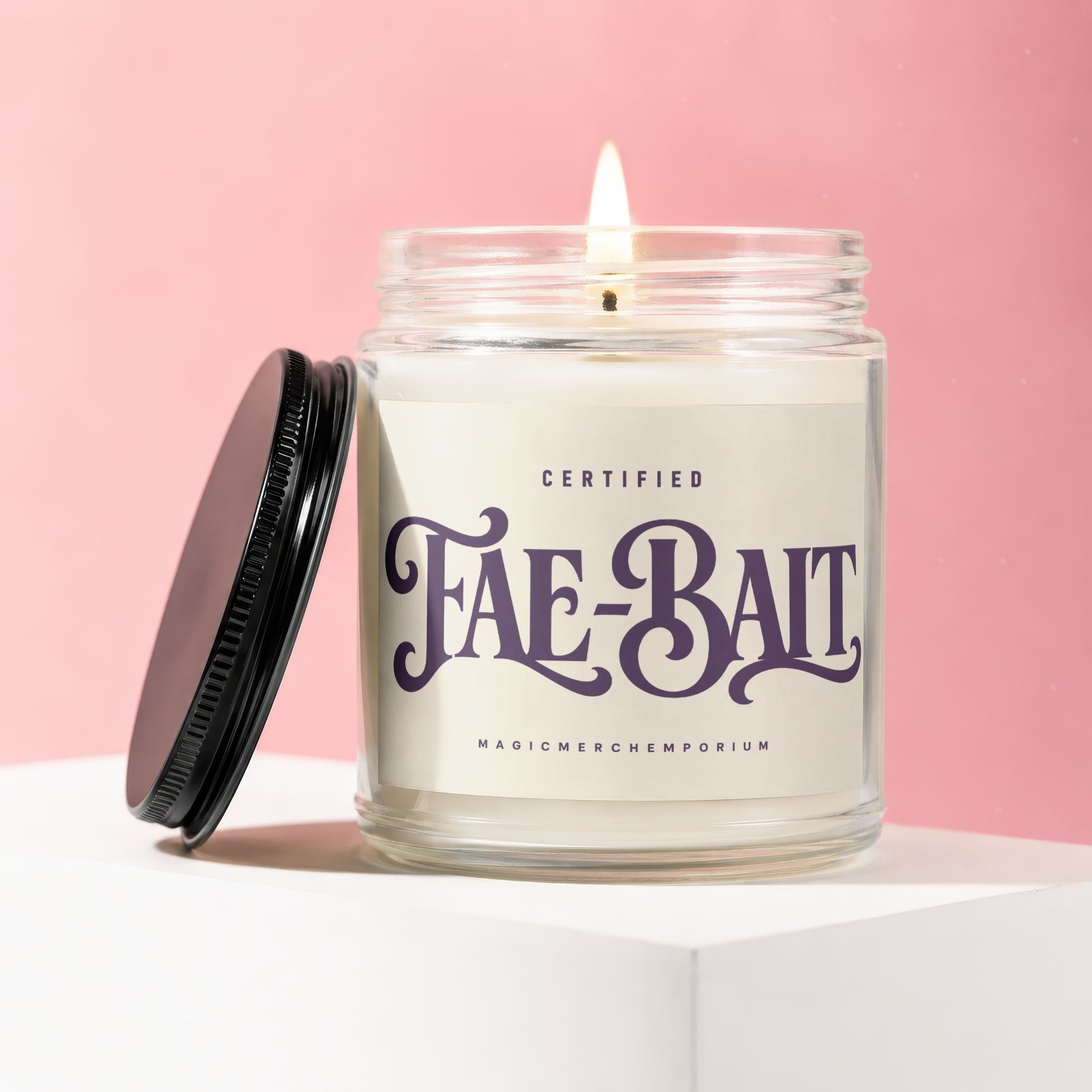 Glass jar candle labeled "Fae-Bait Certified MagicMerchemporeum" with lit wick and black lid.