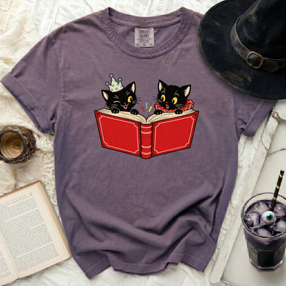 Two black kittens reading an open red book, one wearing a party hat.