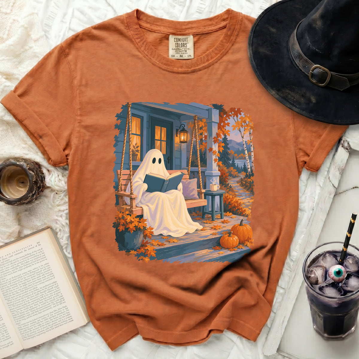Ghost reading book on porch swing with pumpkins and fall leaves.