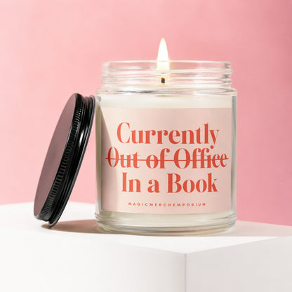 Candle with lit wick, reads "Currently Out of Office In a Book" on label.