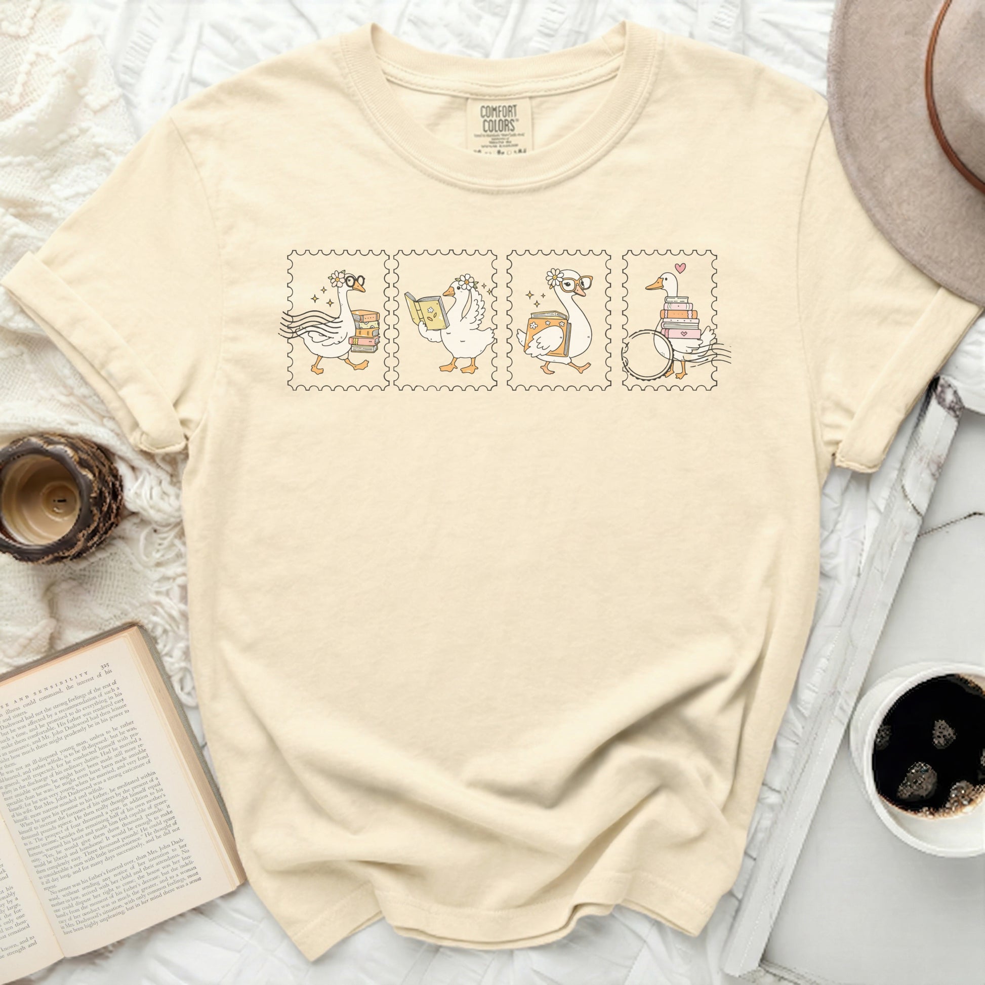 Cream t-shirt with four goose postage stamps reading books.