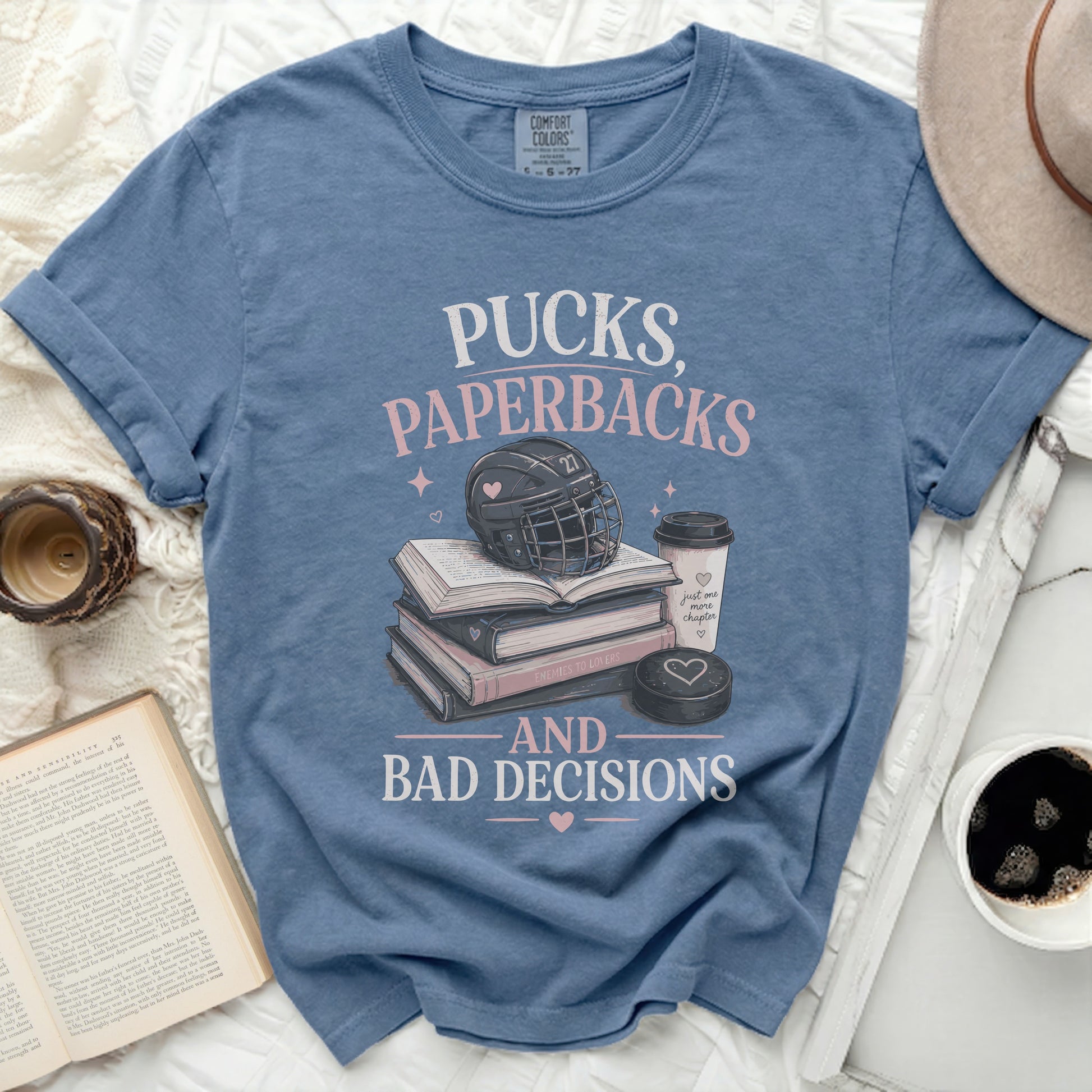 Blue t-shirt with "Pucks, Paperbacks, and Bad Decisions" text, hockey helmet, and books.