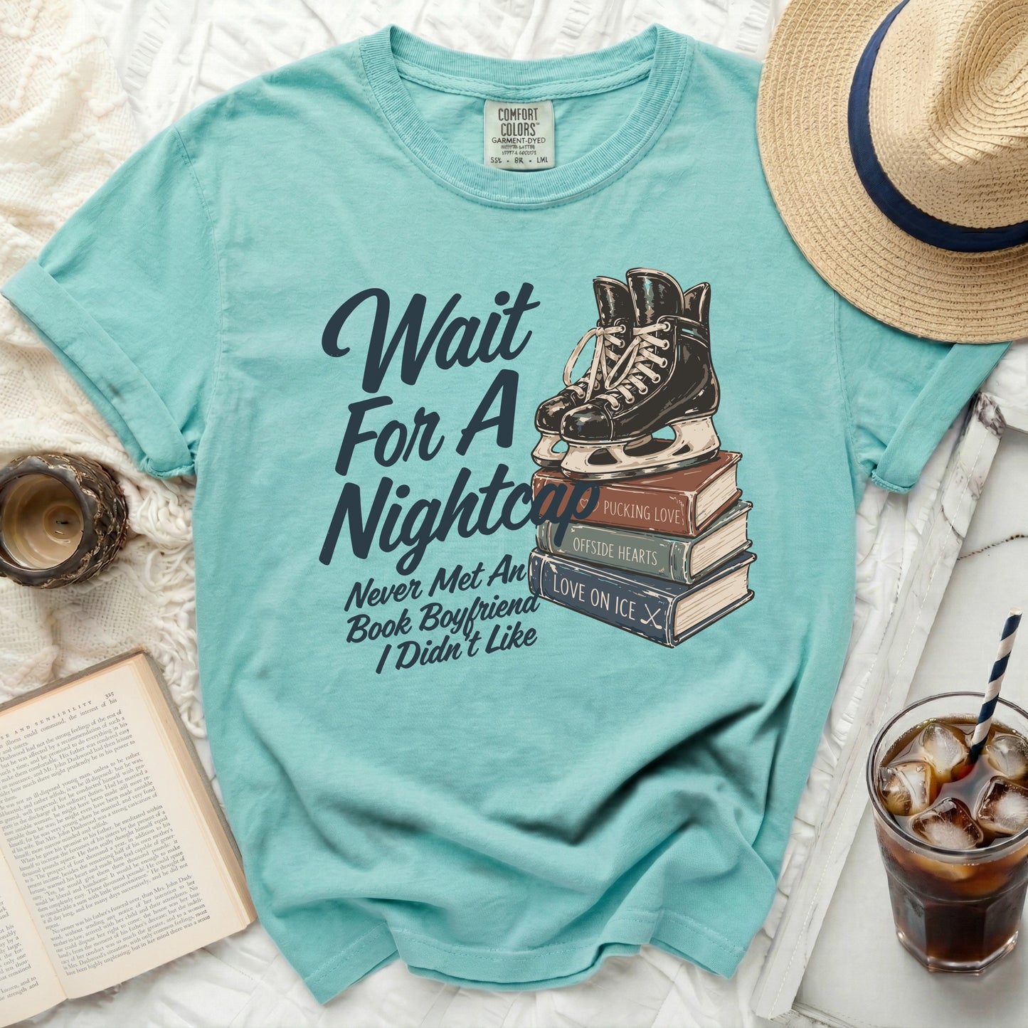 Teal t-shirt with stacked books, ice skates, and "Wait For A Nightcap" graphic.