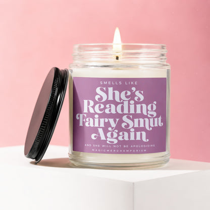 Lit candle in a glass jar with a purple label that reads "Smells Like She's Reading Fairy Smut Again".