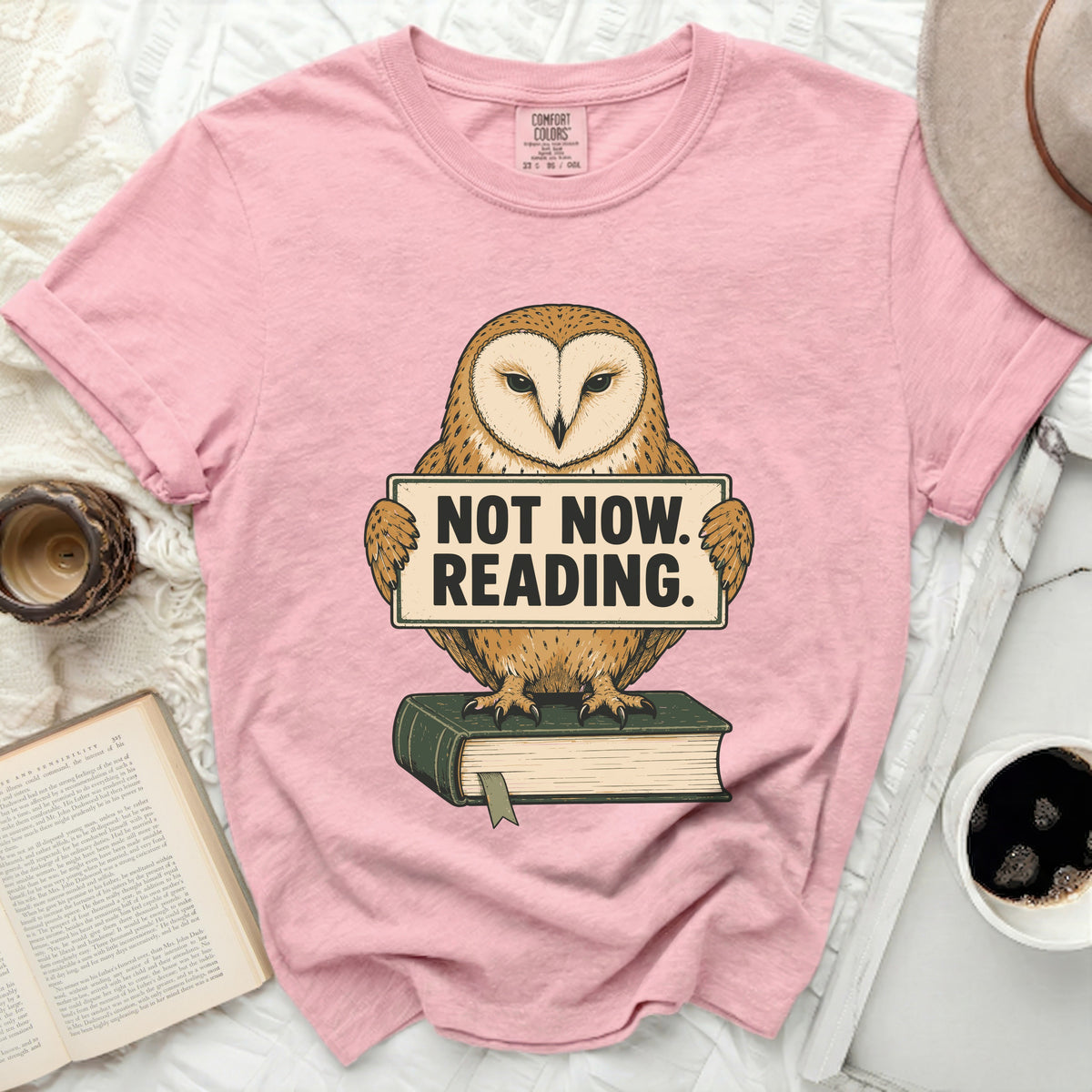 Pink t-shirt with illustration of owl holding "Not Now. Reading." sign on a book.