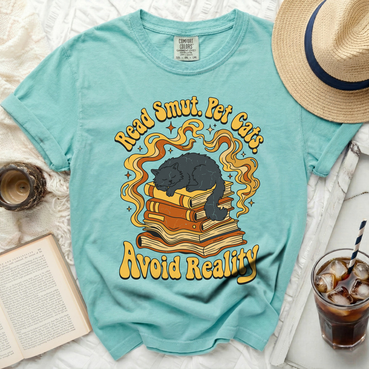 Teal t-shirt with "Read Smut. Pet Cats. Avoid Reality." graphic of a cat on books.