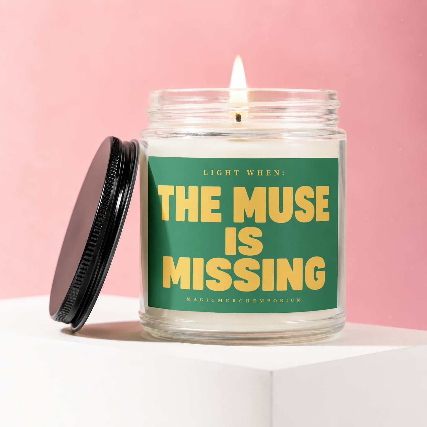 Burning candle in a glass jar with green label that reads "Light When: The Muse is Missing".