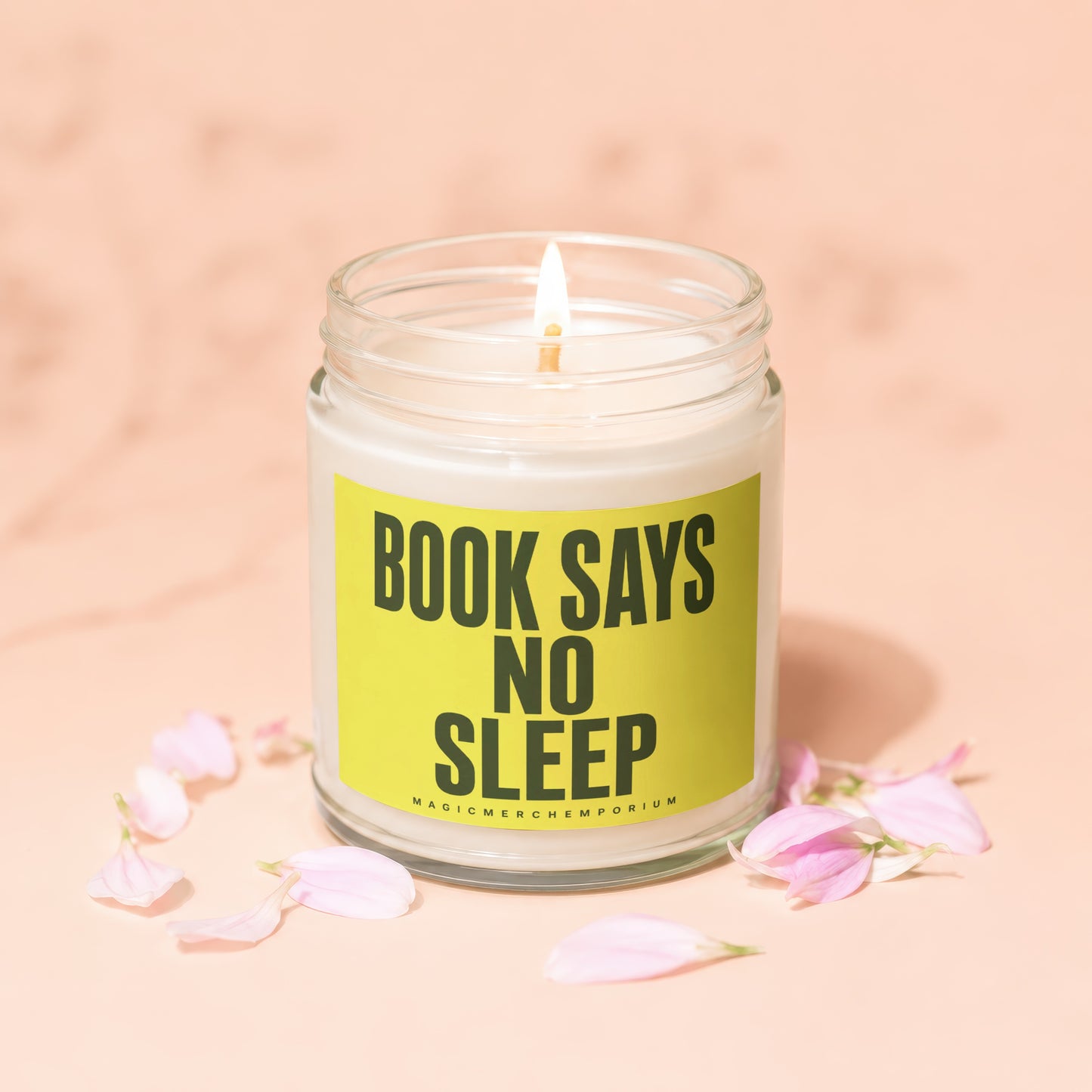 Candle with "Book Says No Sleep" text on a yellow label, surrounded by pink petals.