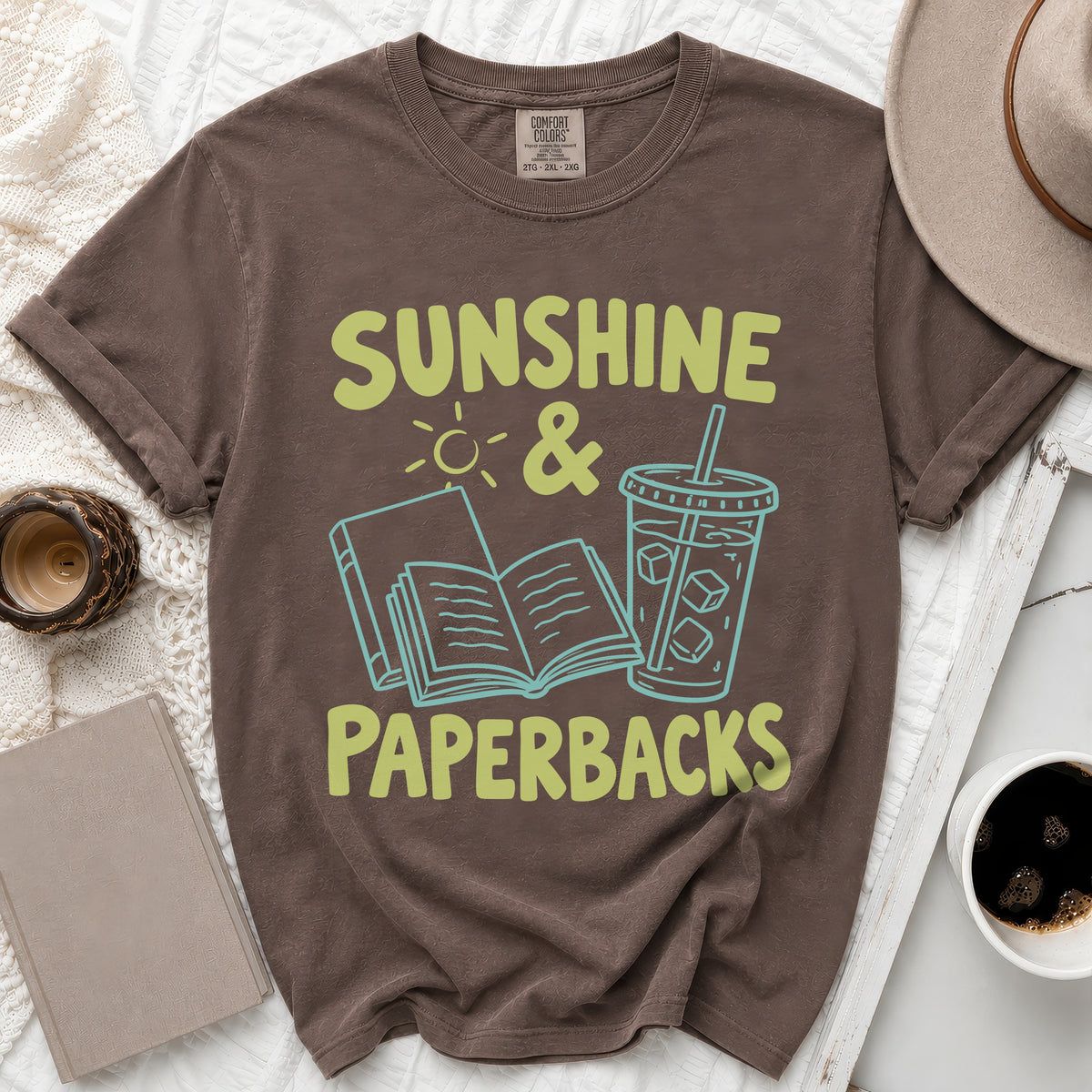 Brown t-shirt with "Sunshine & Paperbacks" text, book, sun, and iced drink graphics.