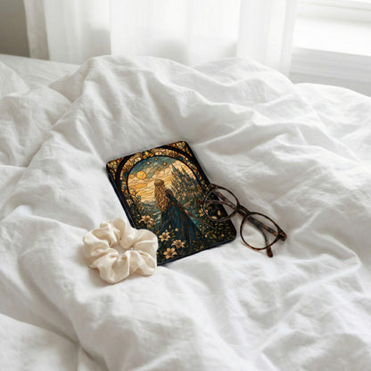 E-reader with stained glass castle design, glasses, and scrunchie on white bedding.