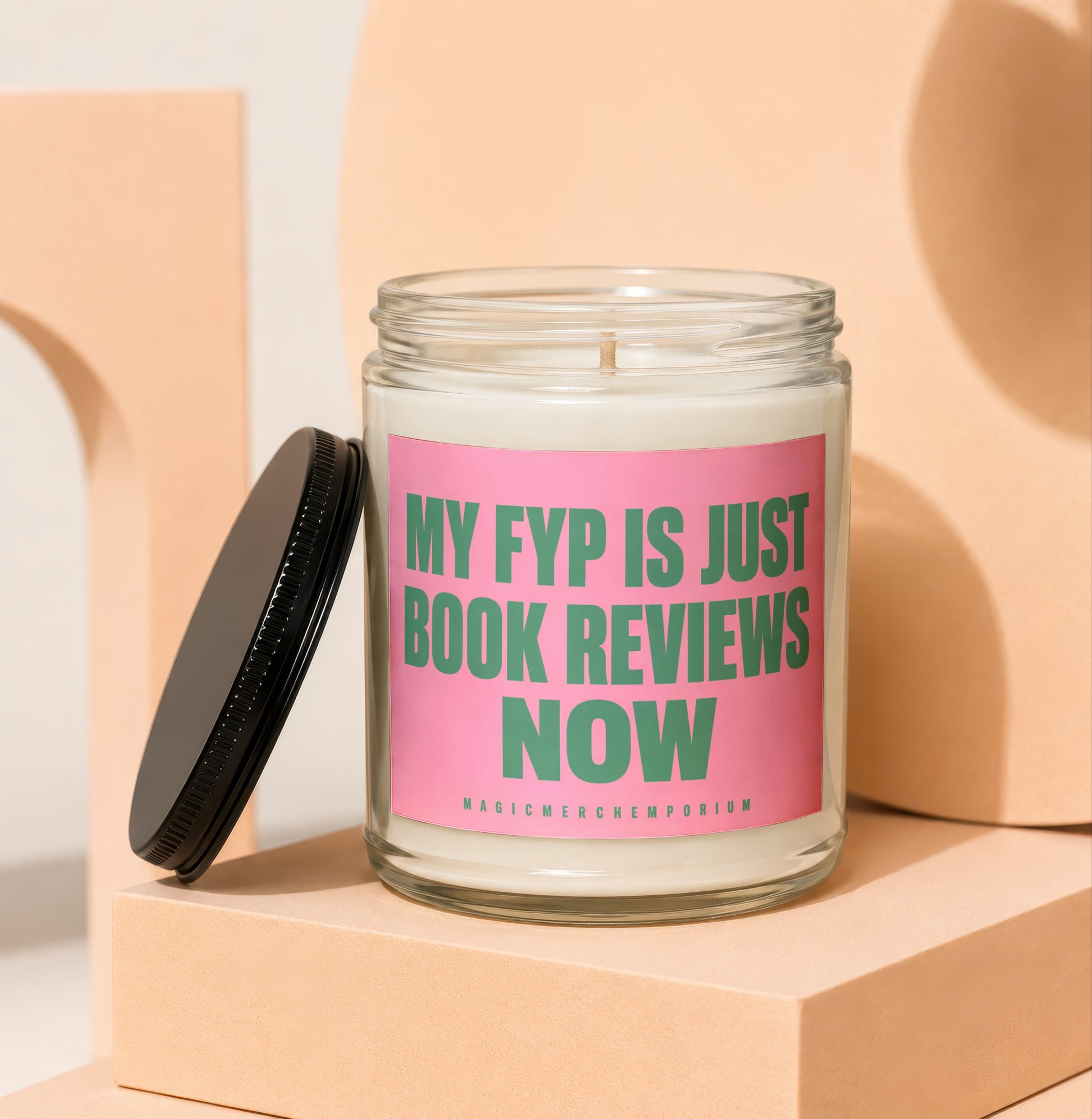 Glass candle with pink label that reads "MY FYP IS JUST BOOK REVIEWS NOW" and smaller text "MAGICMERCH...EMPORIUM".