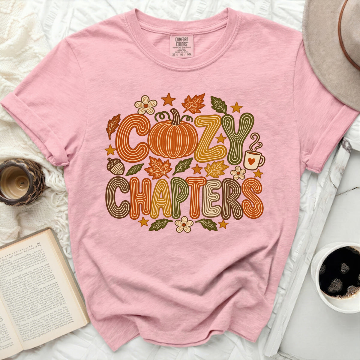 Pink t-shirt with "COZY CHAPTERS" text and fall graphics.