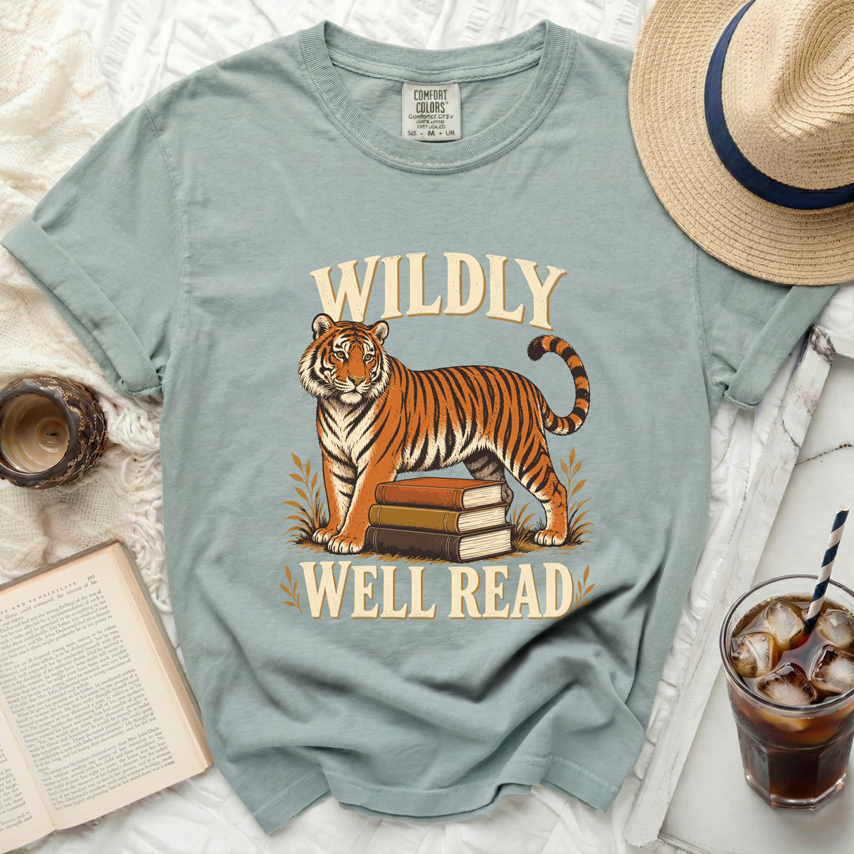 Light blue t-shirt with tiger and books graphic, text reads "WILDLY WELL READ".