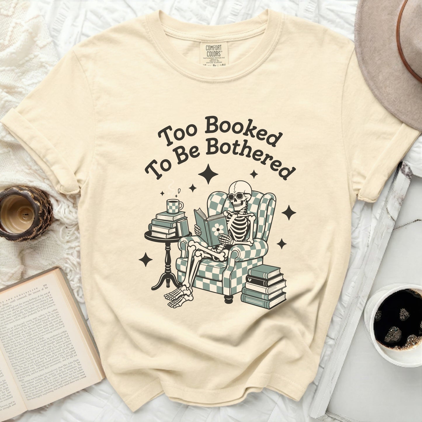 Skeleton reading book in chair with text "Too Booked To Be Bothered."