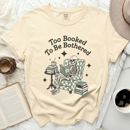 Skeleton reading book in chair with text "Too Booked To Be Bothered."