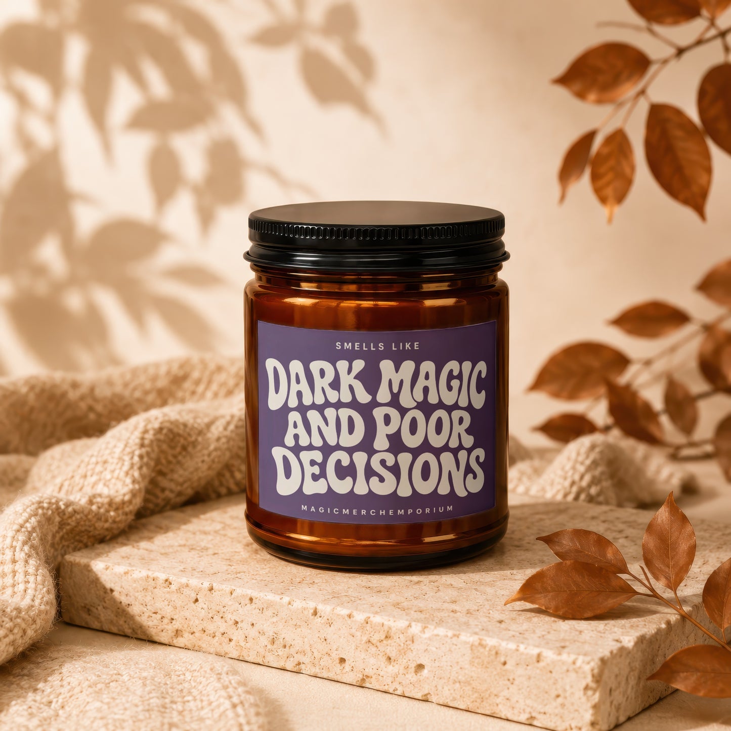 Candle labelled "Dark Magic and Poor Decisions" with a textured knit blanket and fall leaves.