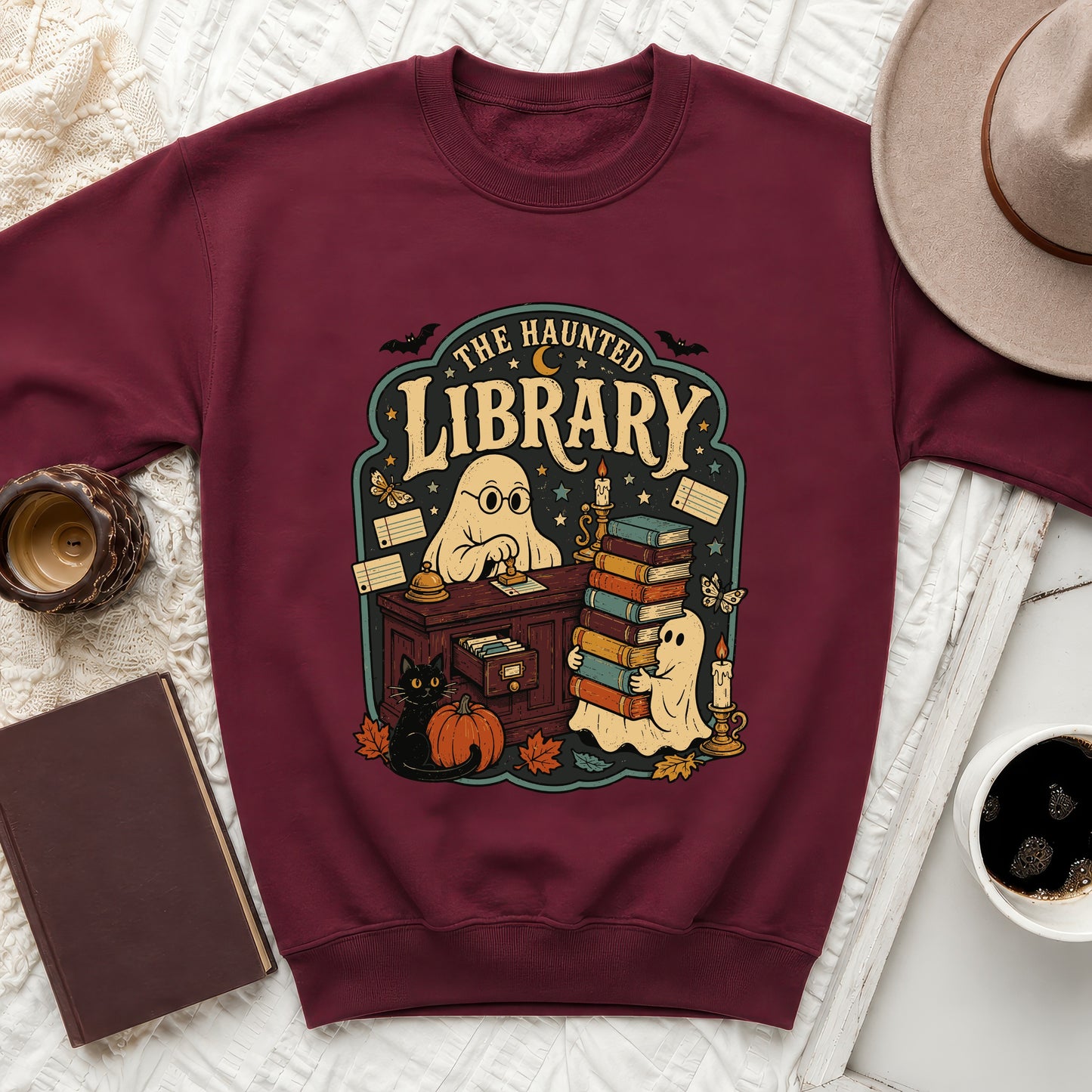 Maroon sweatshirt with "The Haunted Library" graphic featuring ghosts, books, and fall decor.