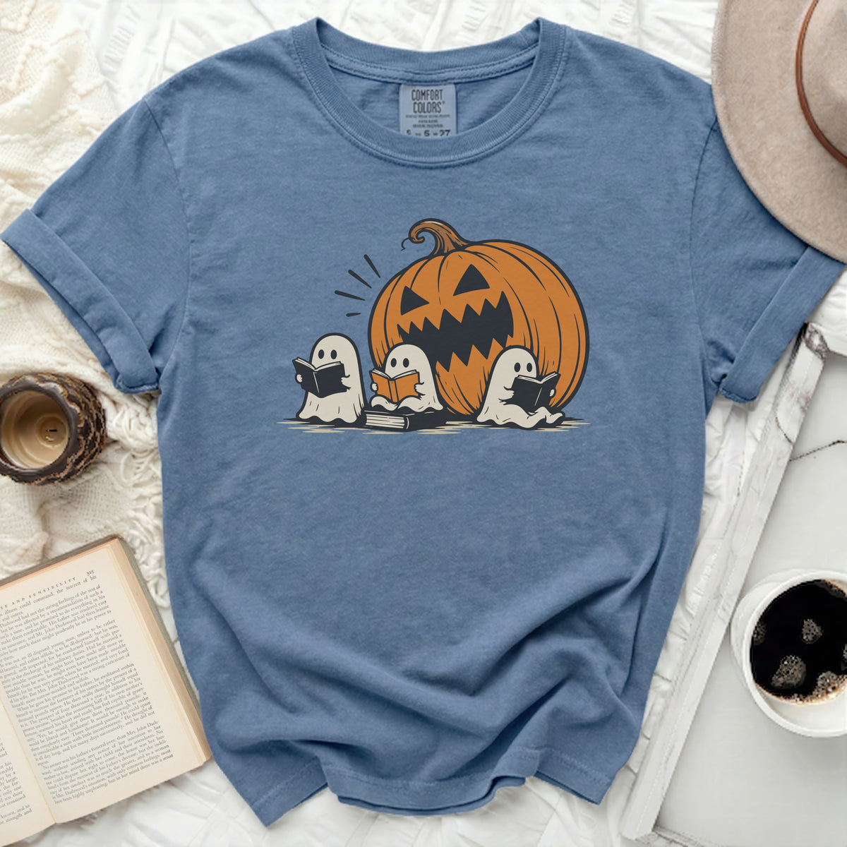Three ghosts read books in front of a jack-o'-lantern on a blue t-shirt.