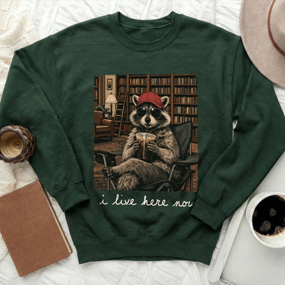 Green sweatshirt with raccoon graphic in library, holding drink, wearing hat and sunglasses.