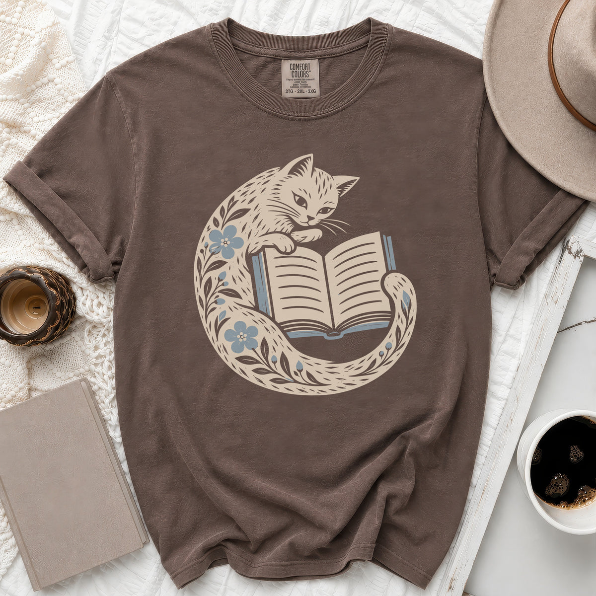 Brown t-shirt with a cat reading a book design and floral accents.