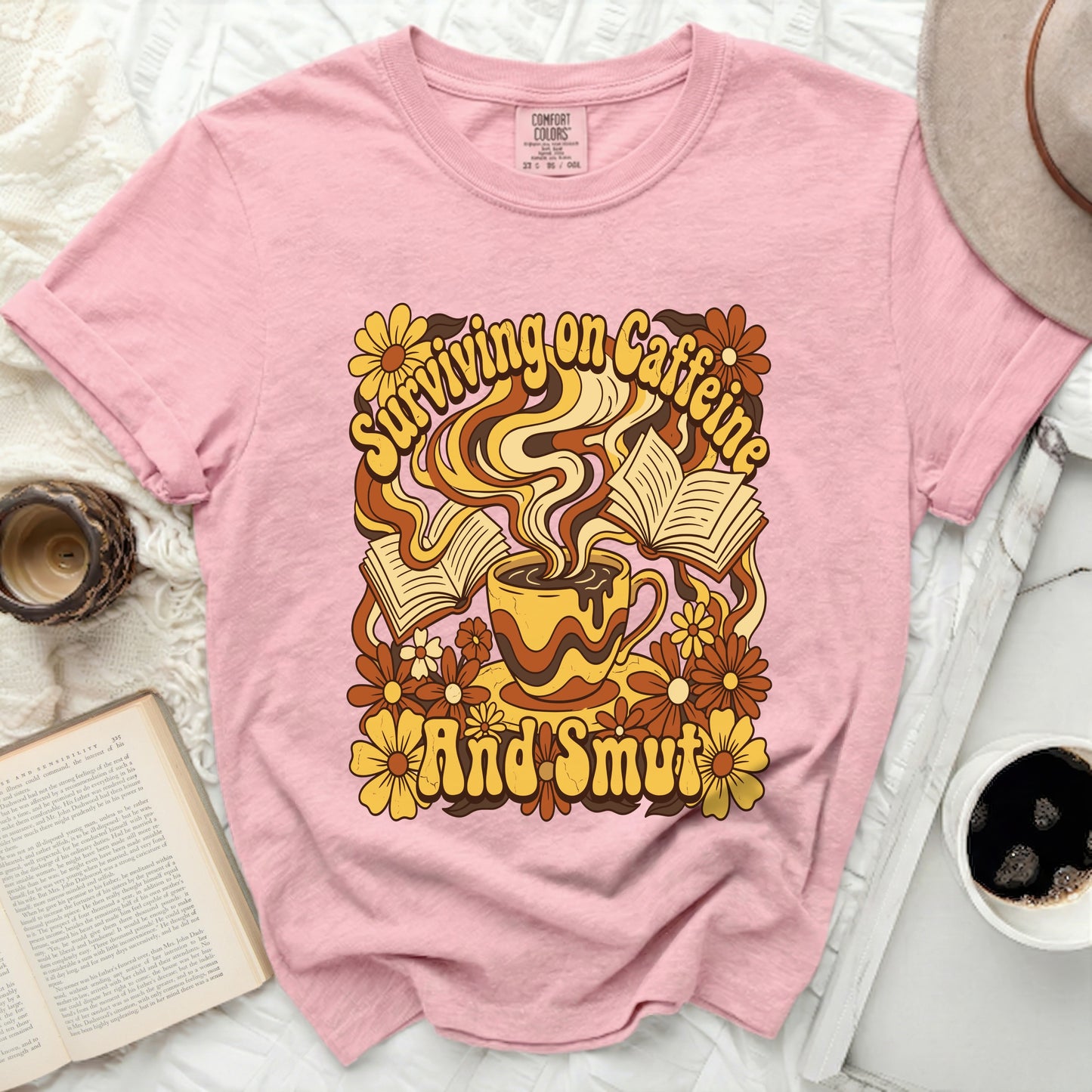 Pink t-shirt with "Surviving on Caffeine and Smut" graphic.