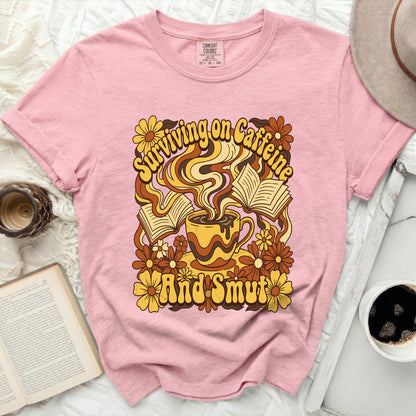 Pink t-shirt with "Surviving on Caffeine and Smut" graphic.