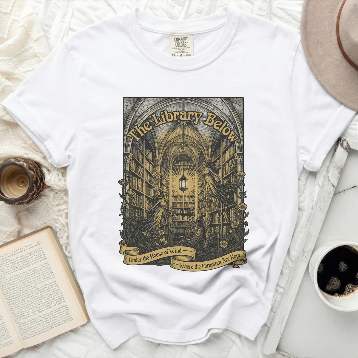 White t-shirt with "The Library Below - Under the House of Wind - Where the Forgotten Are Kept" graphic.