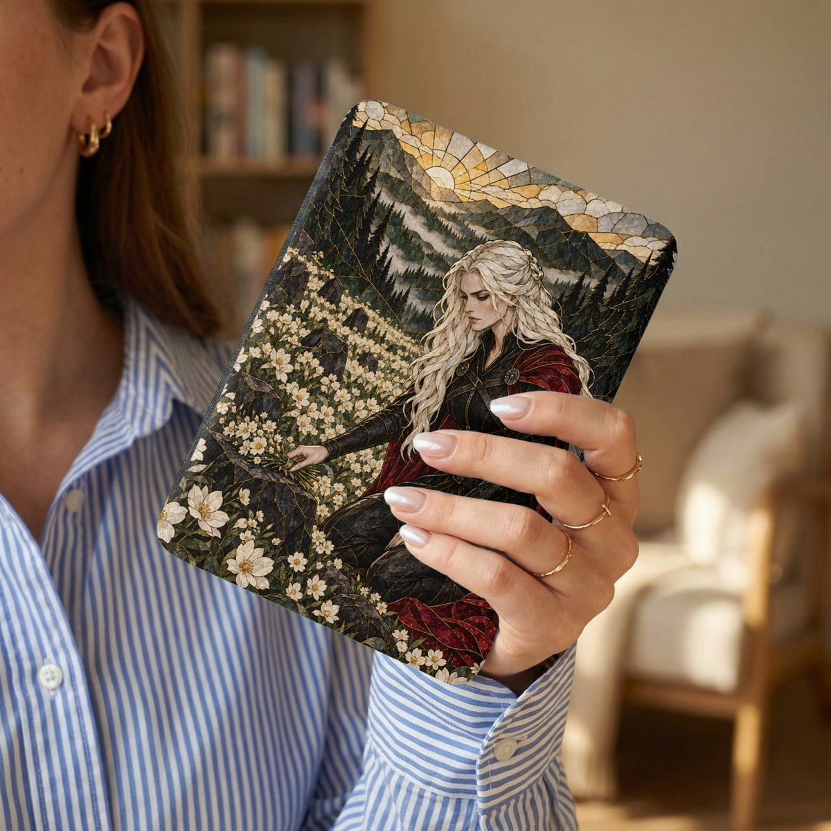 Woman holds a journal featuring a woman in a cape with a forest and mountain landscape.
