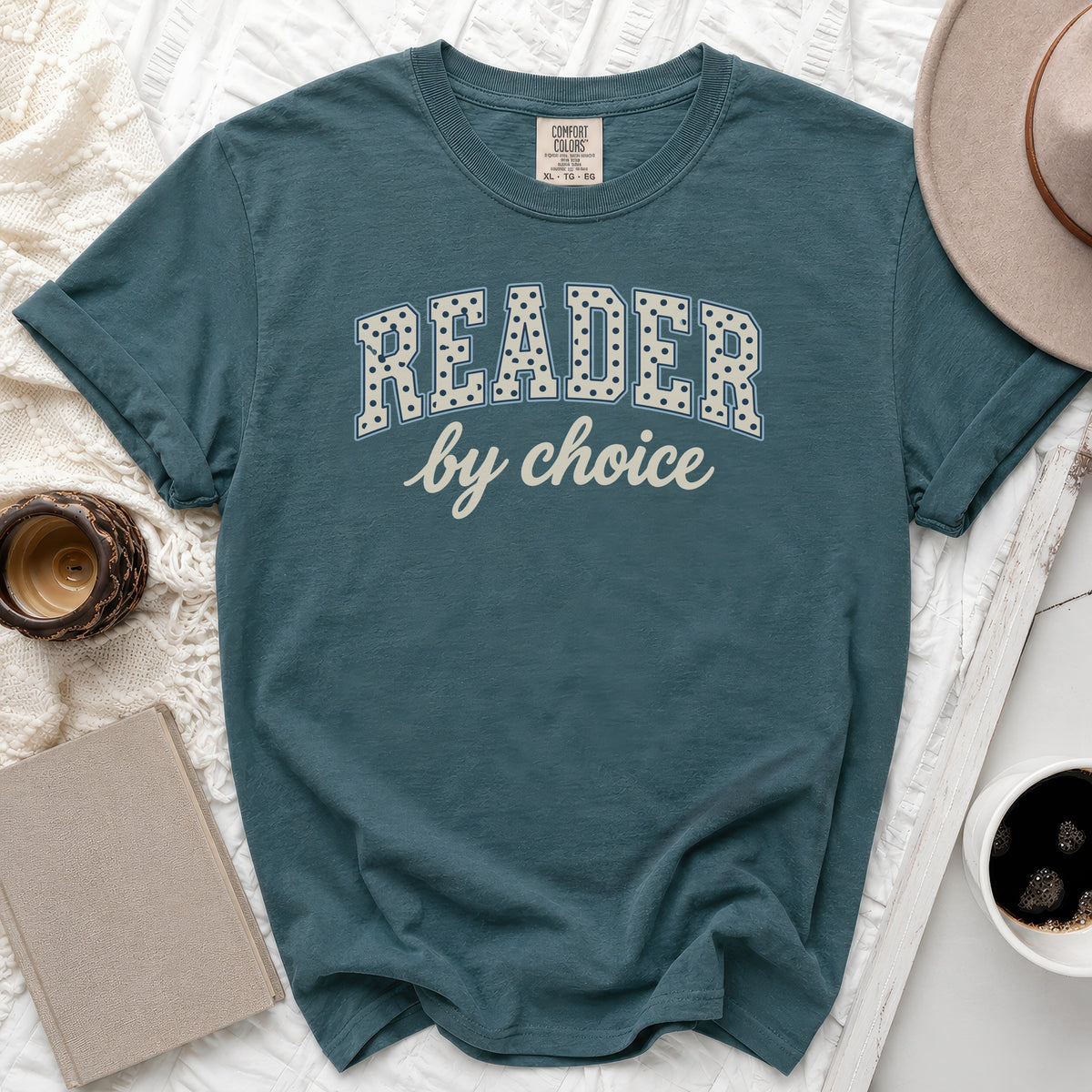 Teal t-shirt with "READER by choice" text and a beige hat.