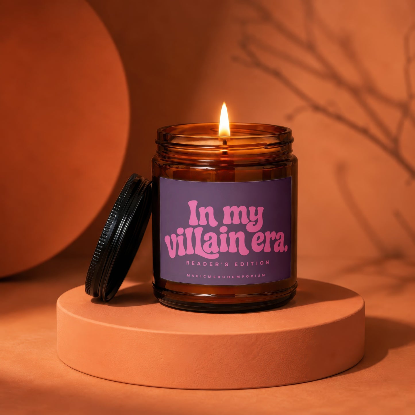 Amber candle with lit flame, purple label reading "In my villain era. READER'S EDITION MAGICMERCH.EMPORIUM".