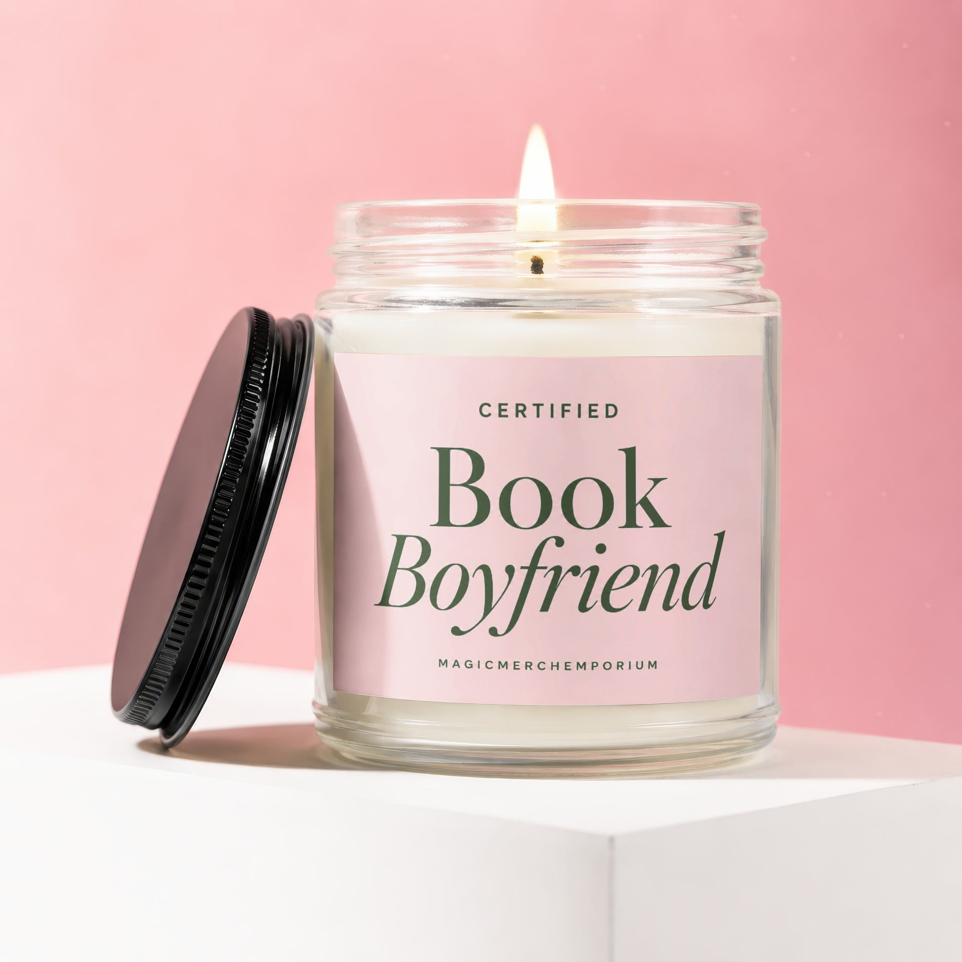 Candle with a lit wick on a white pedestal with a pink background, labeled "Certified Book Boyfriend".