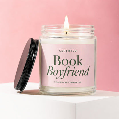 Candle with a lit wick on a white pedestal with a pink background, labeled "Certified Book Boyfriend".