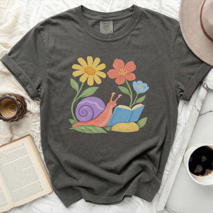 Grey t-shirt with a graphic of a snail reading a book among flowers.