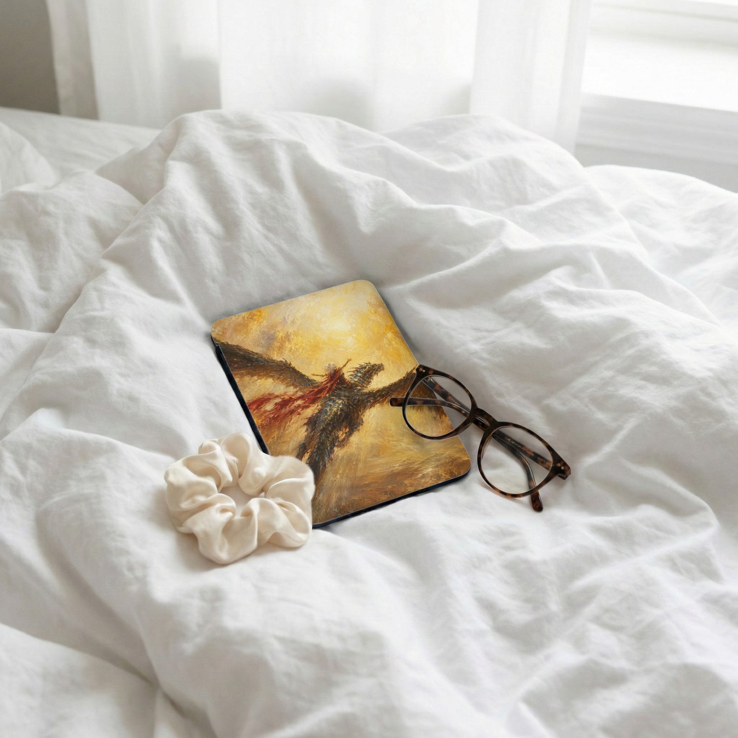 Mousepad with dragon rider artwork, scrunchie, and glasses on white linens.