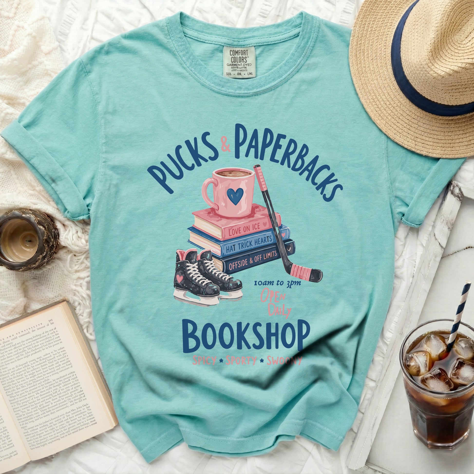 Aqua t-shirt with "Pucks & Paperbacks" text, hockey skates, and books.