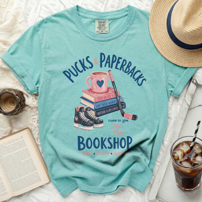 Aqua t-shirt with "Pucks & Paperbacks" text, hockey skates, and books.