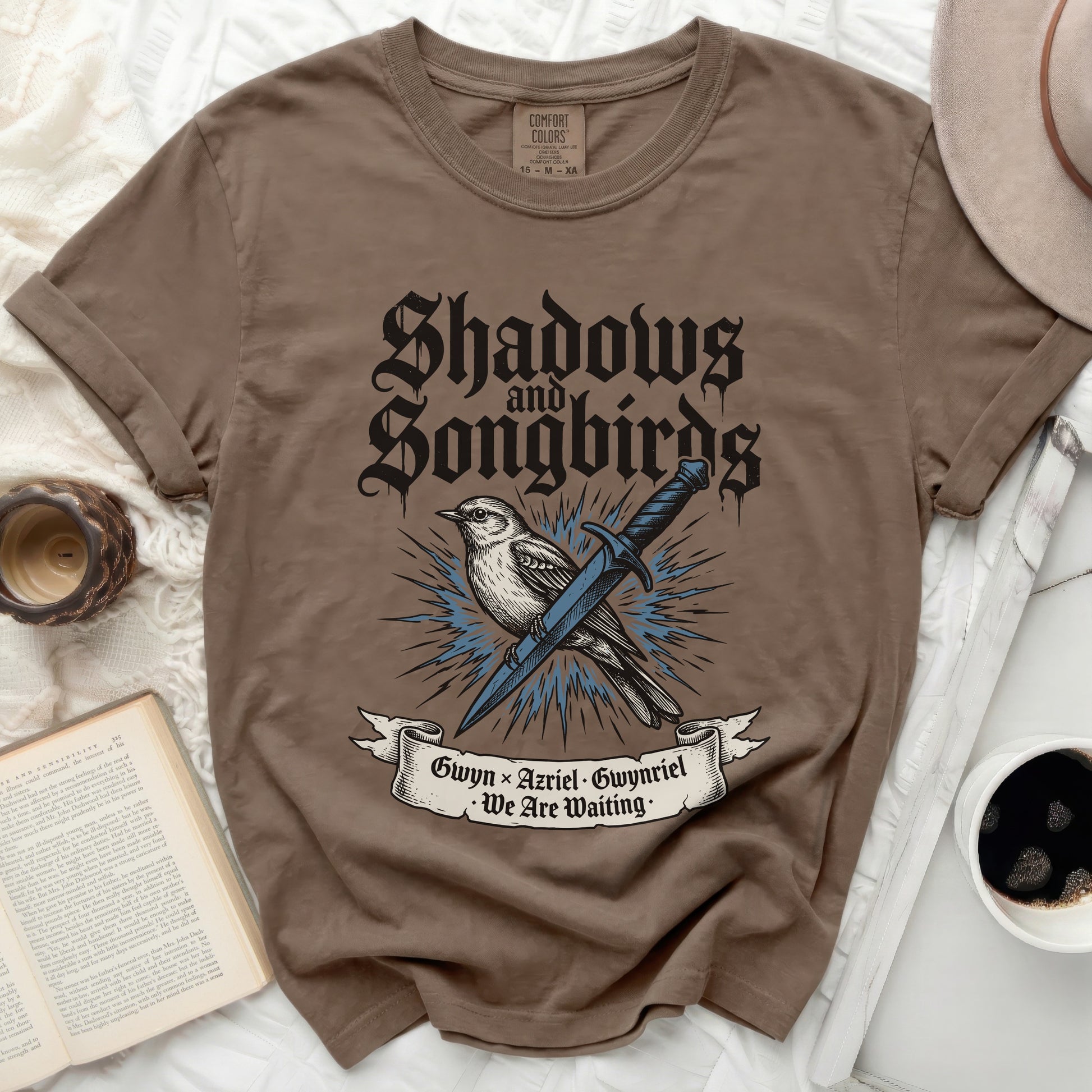 Brown t-shirt with "Shadows and Songbirds" text, sword, and birds.