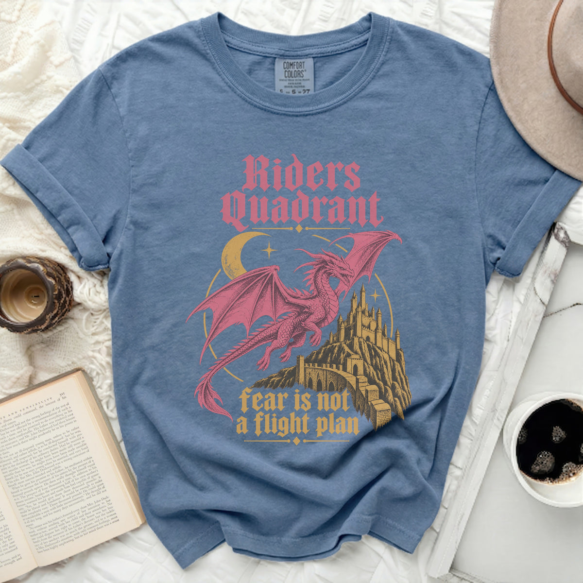 Blue t-shirt with pink dragon, castle, moon, and text "Riders Quadrant fear is not a flight plan".