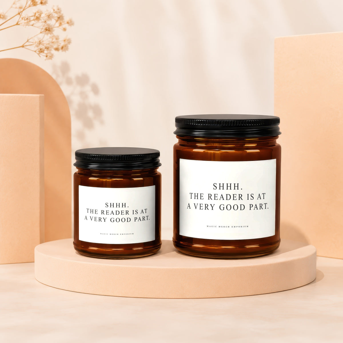 Two amber glass candles with black lids, featuring labels that read "SHHH. THE READER IS AT A VERY GOOD PART."