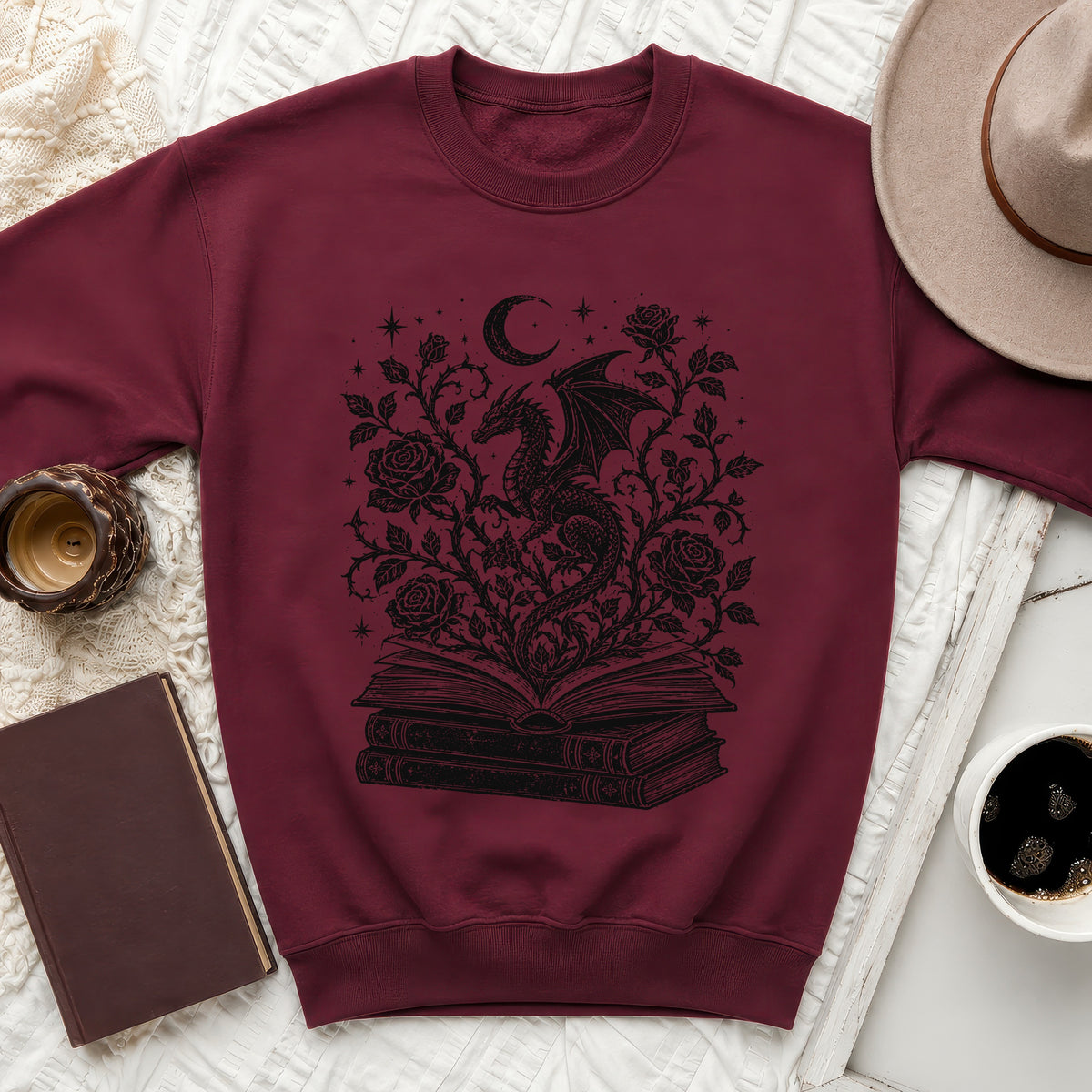 Maroon sweatshirt with black dragon, roses, moon, and stars design on open books.