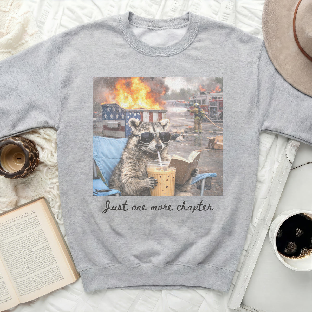 Gray sweatshirt with raccoon wearing sunglasses, drinking coffee, and reading a book with text.