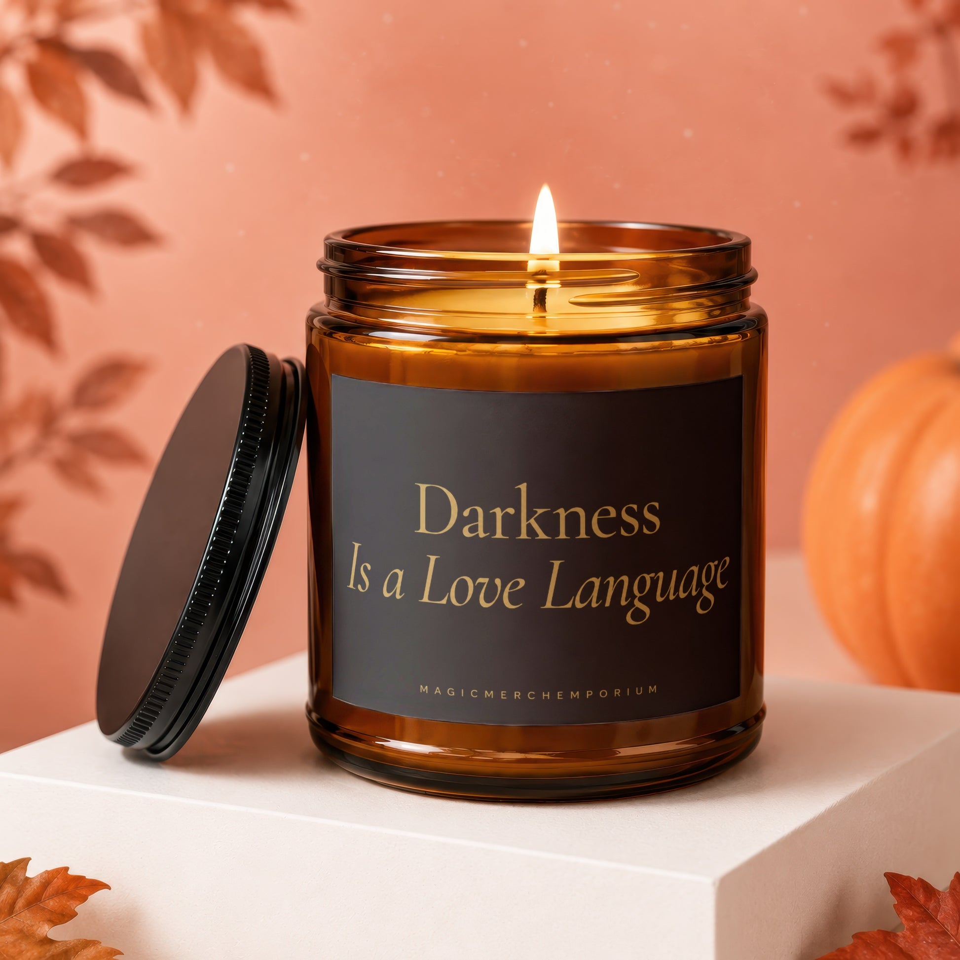 Amber jar candle with lit flame, lid off, displaying "Darkness Is a Love Language" text.