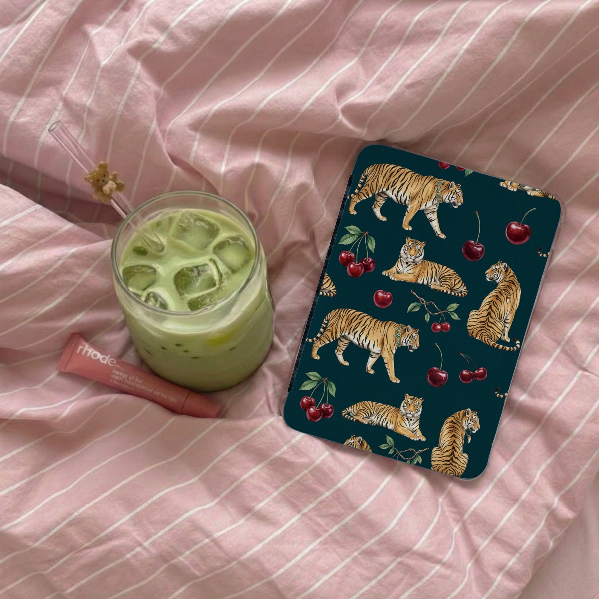 Dark teal phone case with tiger and cherry pattern on pink striped bedding.
