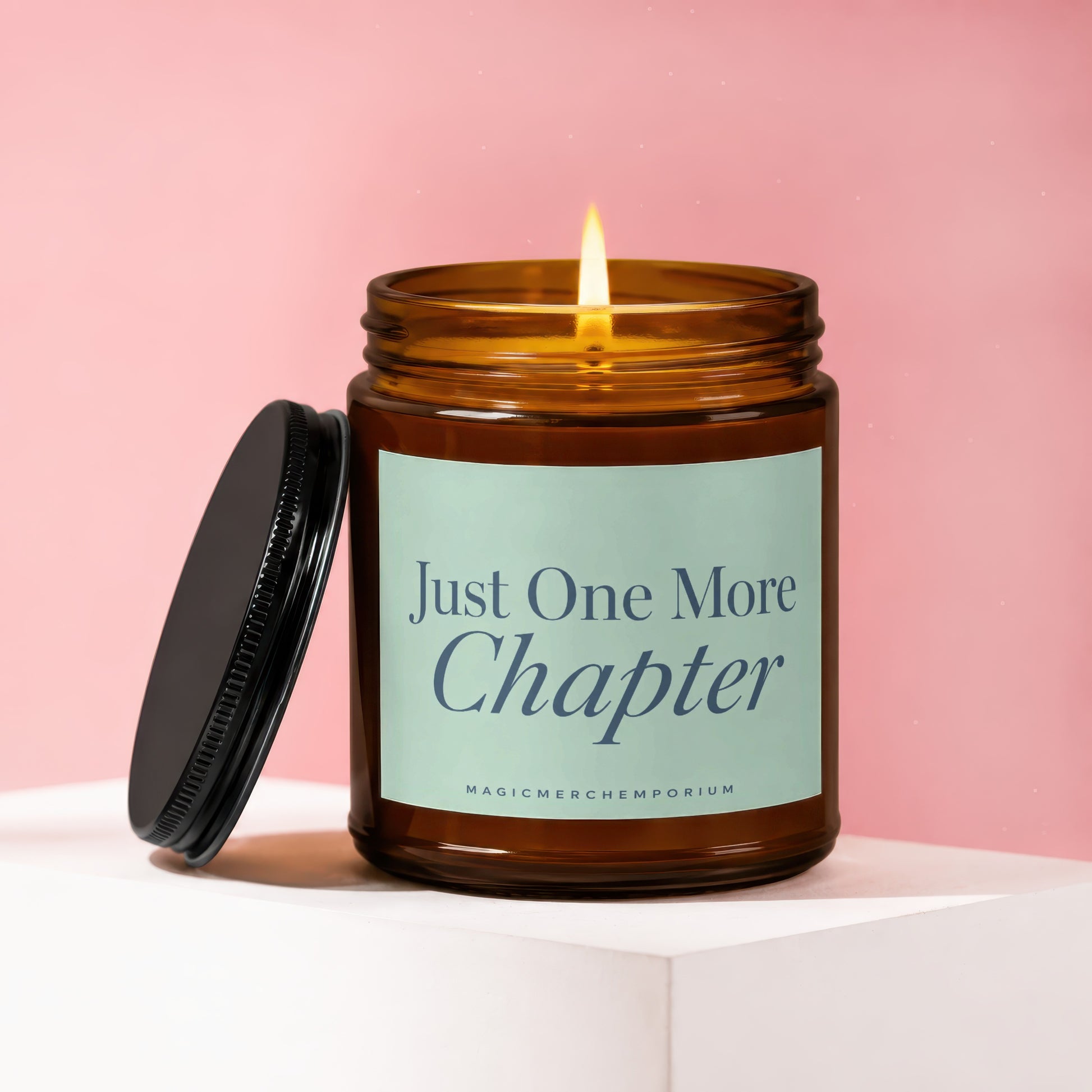 Amber glass candle with lit wick and lid off, text "Just One More Chapter".