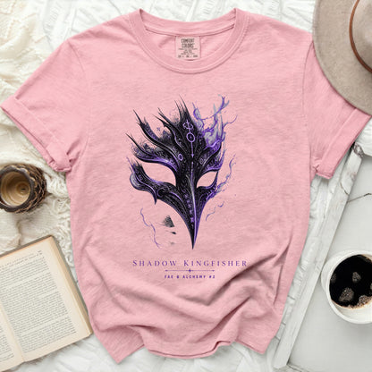 Pink t-shirt with a black and purple feathered mask graphic and text.