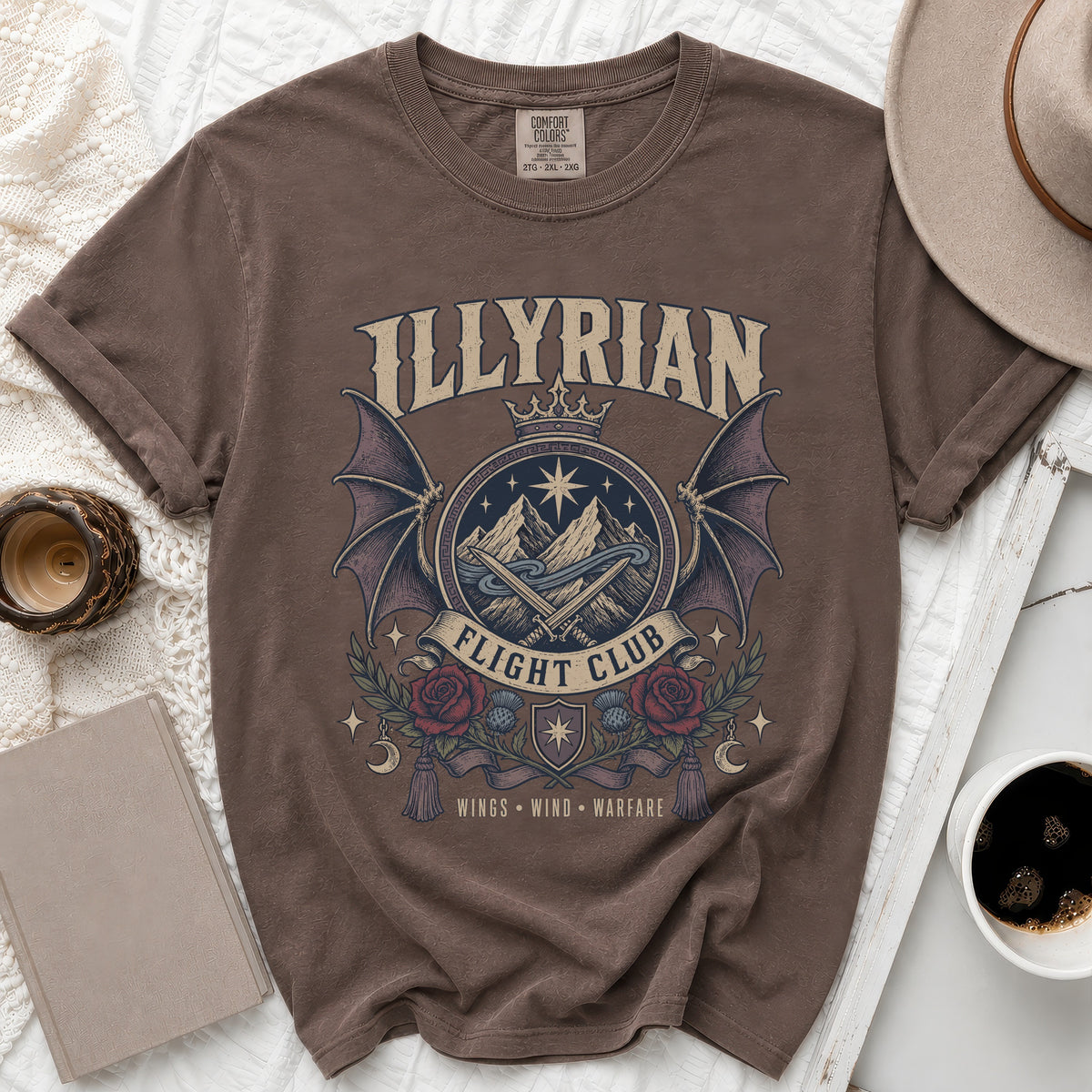 Brown t-shirt with a circular graphic featuring mountains, wings, roses, and the text "ILLYRIAN FLIGHT CLUB".